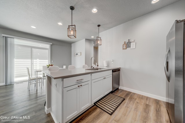 kitchen with a sink, a textured ceiling, light wood-style flooring, stainless steel appliances, and a peninsula