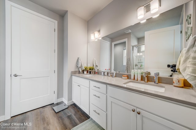 bathroom with a sink, double vanity, baseboards, a shower stall, and wood finished floors