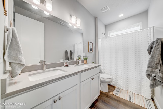 full bathroom with a sink, double vanity, toilet, and wood finished floors