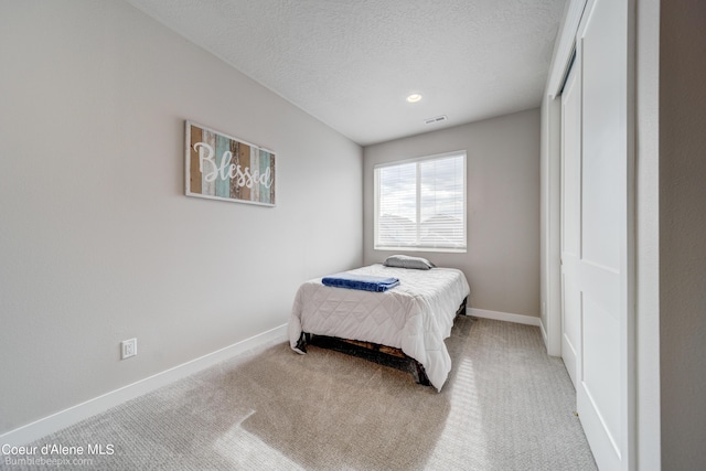 bedroom featuring a textured ceiling, baseboards, visible vents, and light carpet