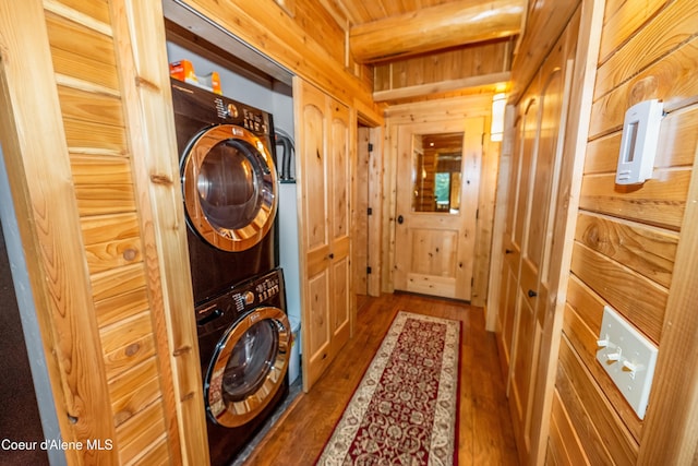 laundry area with laundry area, wooden walls, stacked washer / drying machine, and dark wood-style floors