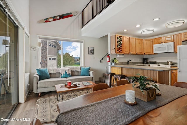 kitchen featuring light brown cabinetry, white appliances, a high ceiling, recessed lighting, and light wood finished floors