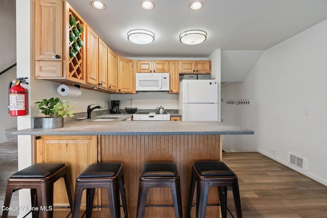 kitchen with visible vents, a sink, a peninsula, light brown cabinets, and white appliances