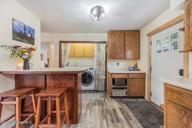 820 Plum Ln, Saint Maries, ID 83861 - kitchen featuring light countertops, a breakfast bar area, brown cabinetry, washer / clothes dryer, and wood finished floors