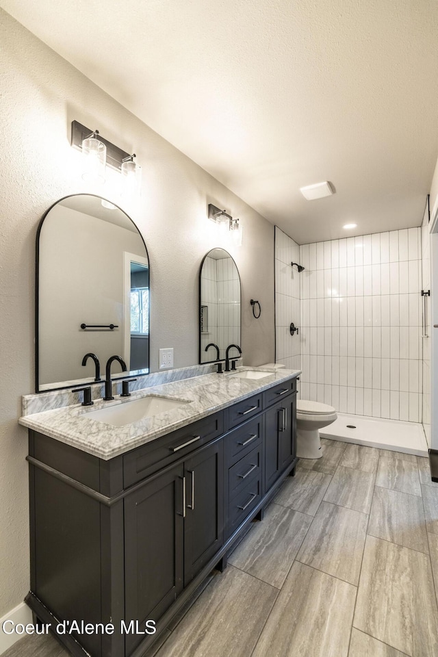 full bathroom with double vanity, toilet, a tile shower, and a sink