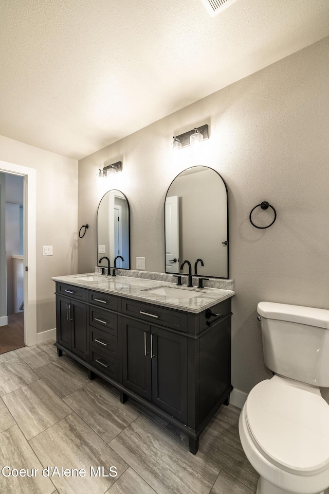 bathroom featuring double vanity, baseboards, toilet, and a sink
