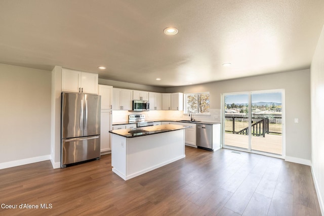 kitchen with dark wood-style flooring, appliances with stainless steel finishes, a sink, white cabinetry, and a kitchen island