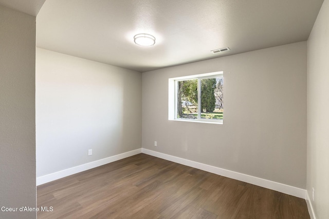 empty room featuring baseboards, dark wood-type flooring, and visible vents