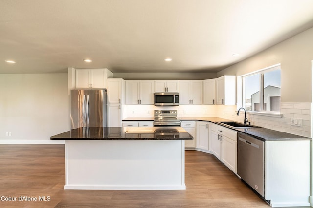 kitchen with a sink, stainless steel appliances, white cabinetry, backsplash, and a kitchen island