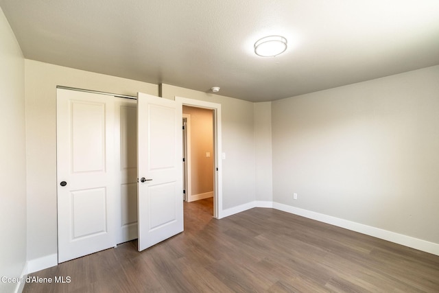 unfurnished bedroom with dark wood-style flooring, baseboards, and a closet