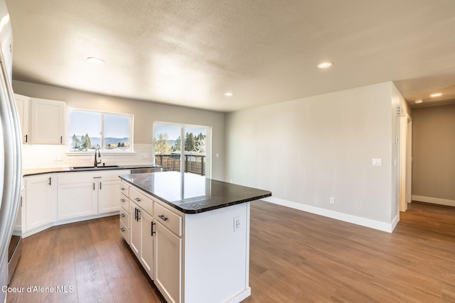 kitchen featuring decorative backsplash, wood finished floors, a center island, white cabinetry, and a sink