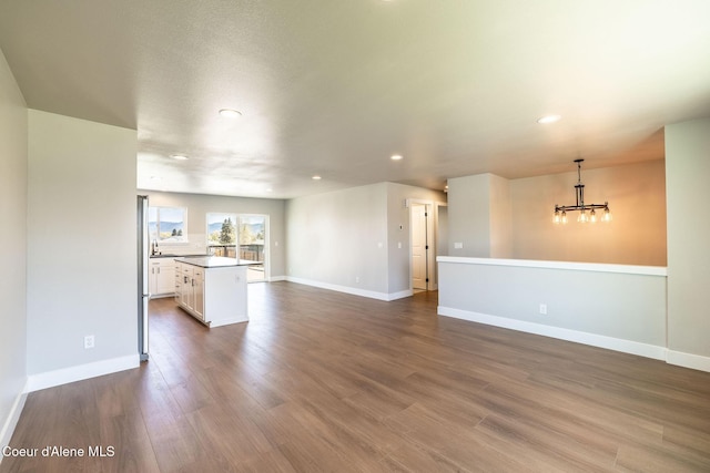 unfurnished living room featuring an inviting chandelier, baseboards, recessed lighting, and dark wood-style floors