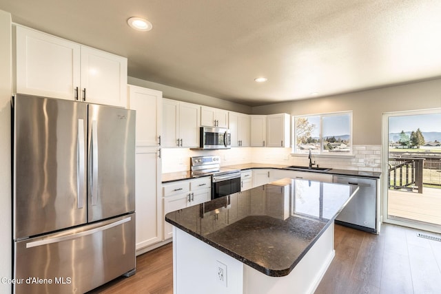 kitchen with decorative backsplash, dark wood-style floors, white cabinets, a sink, and stainless steel appliances