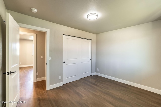 unfurnished bedroom with baseboards, a closet, and dark wood-type flooring
