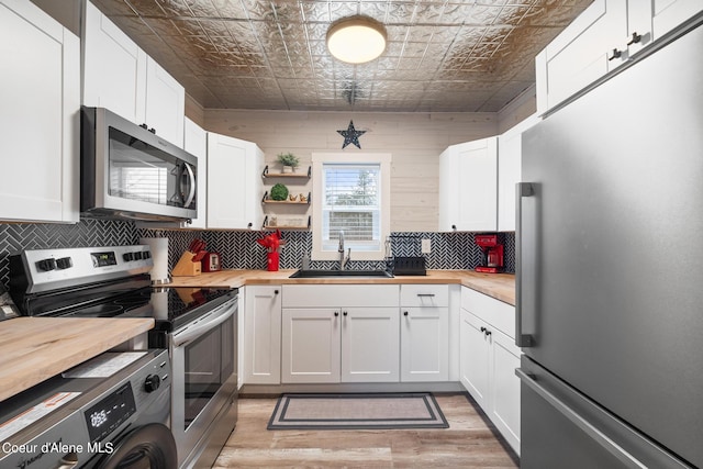 kitchen featuring a sink, an ornate ceiling, stainless steel appliances, washer / dryer, and butcher block counters