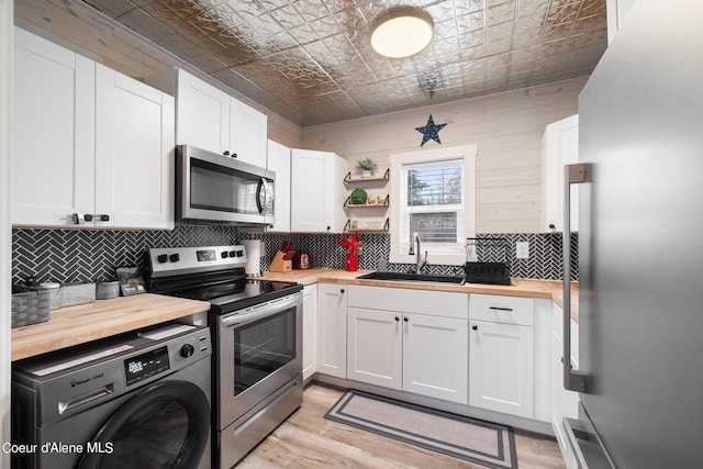 kitchen with butcher block counters, washer / clothes dryer, an ornate ceiling, a sink, and appliances with stainless steel finishes