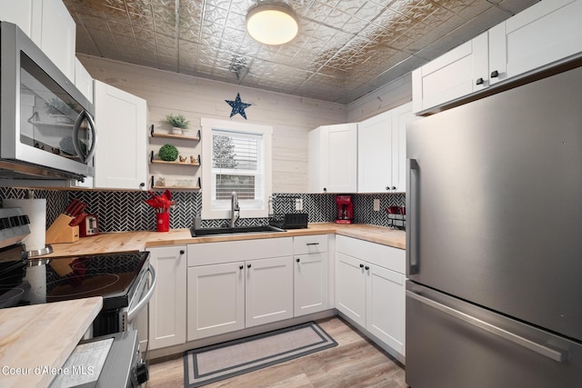 kitchen with a sink, wood counters, appliances with stainless steel finishes, and an ornate ceiling