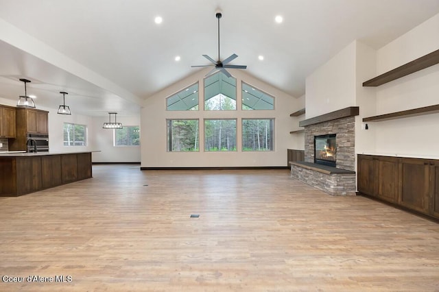 unfurnished living room with high vaulted ceiling, ceiling fan, a fireplace, and light wood-style flooring
