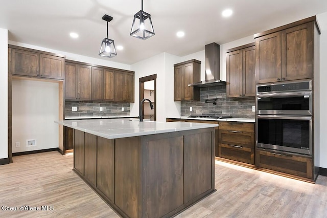 kitchen featuring tasteful backsplash, light wood-style flooring, wall chimney exhaust hood, and double oven
