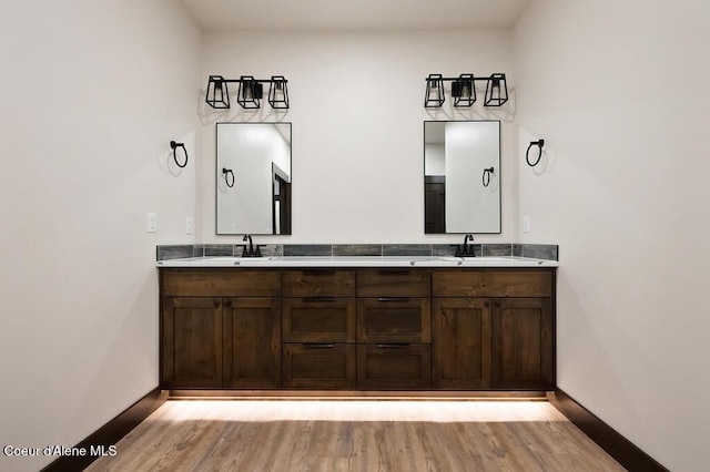 bathroom featuring double vanity, baseboards, wood finished floors, and a sink