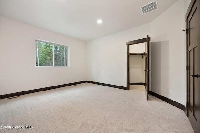 unfurnished bedroom featuring baseboards, a walk in closet, light colored carpet, and visible vents