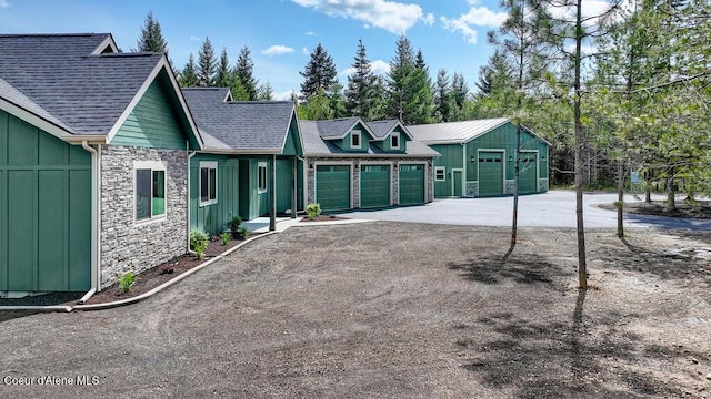 view of front of property with board and batten siding, an attached garage, aphalt driveway, and stone siding