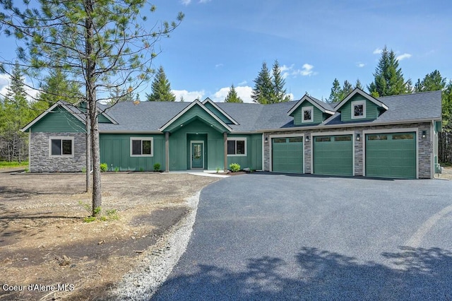 view of front facade with a garage, board and batten siding, stone siding, and aphalt driveway