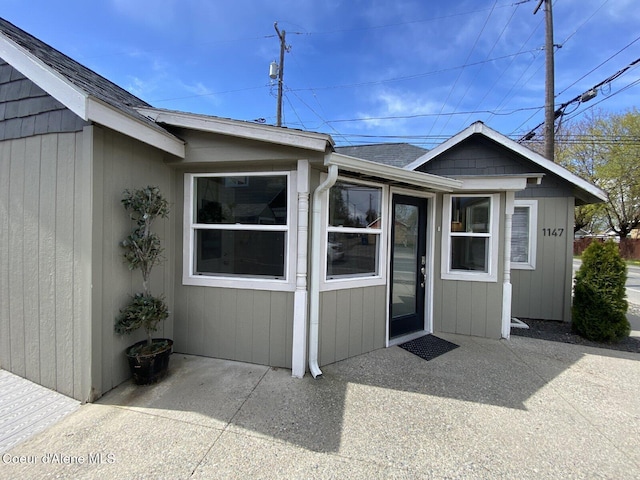 entrance to property featuring roof with shingles and a patio