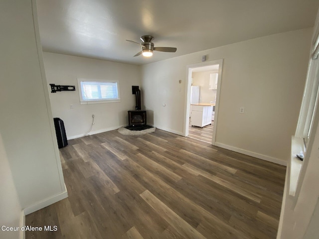 unfurnished living room featuring baseboards, a ceiling fan, a wood stove, and dark wood-style floors