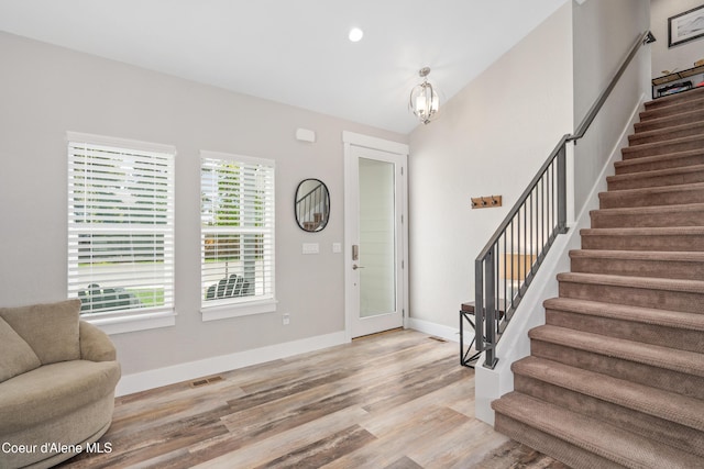 entrance foyer with visible vents, an inviting chandelier, wood finished floors, baseboards, and stairway