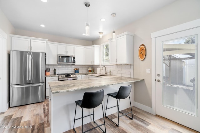 kitchen featuring decorative backsplash, a peninsula, white cabinetry, a sink, and stainless steel appliances