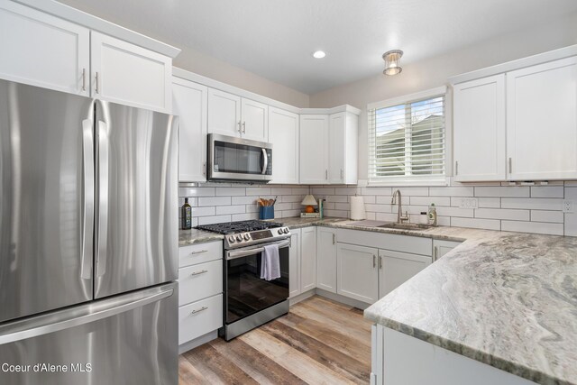 kitchen with backsplash, stainless steel appliances, white cabinetry, and a sink