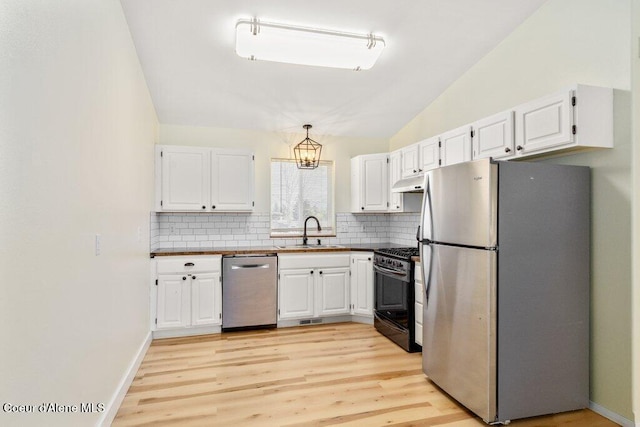 kitchen with a sink, appliances with stainless steel finishes, under cabinet range hood, and tasteful backsplash