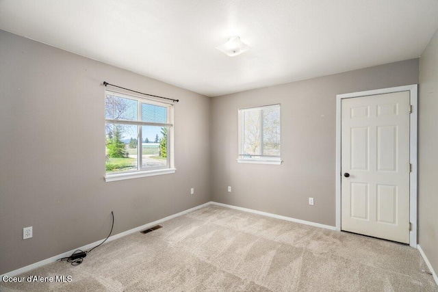 carpeted empty room featuring a healthy amount of sunlight, baseboards, and visible vents