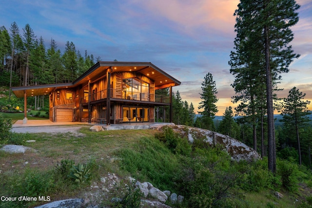 172 Elk Hills Rd, Sandpoint, ID 83864 - back of house at dusk featuring gravel driveway, a balcony, and a garage