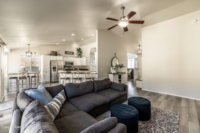 living area featuring wood finished floors, baseboards, high vaulted ceiling, arched walkways, and a ceiling fan