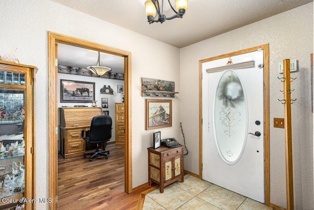 entryway featuring an inviting chandelier, a textured wall, and light wood finished floors