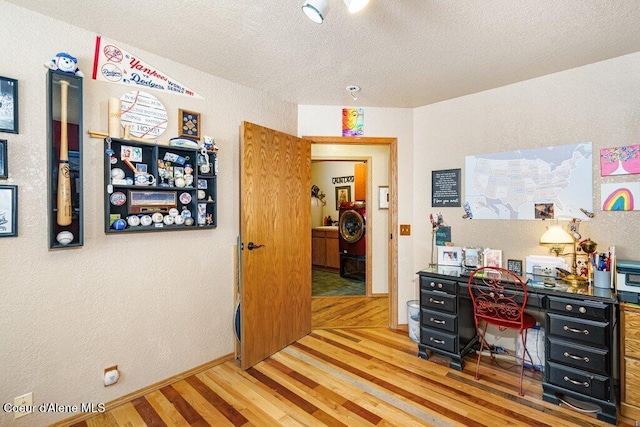 office with a textured wall, washer / dryer, light wood-style floors, baseboards, and a textured ceiling