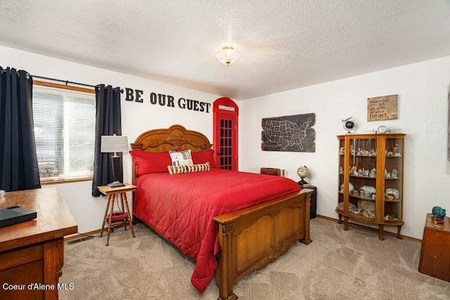 bedroom featuring a textured ceiling, light colored carpet, baseboards, and visible vents