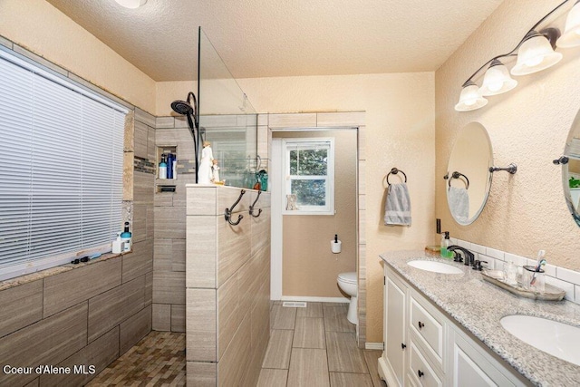full bath with a sink, a textured ceiling, walk in shower, and toilet