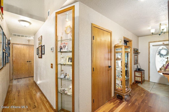 hallway with a textured ceiling, a textured wall, visible vents, and wood finished floors