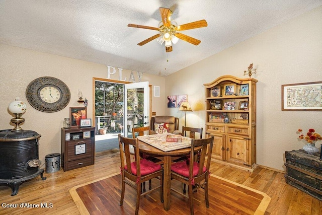 dining area with ceiling fan, a textured ceiling, lofted ceiling, a textured wall, and light wood-style flooring
