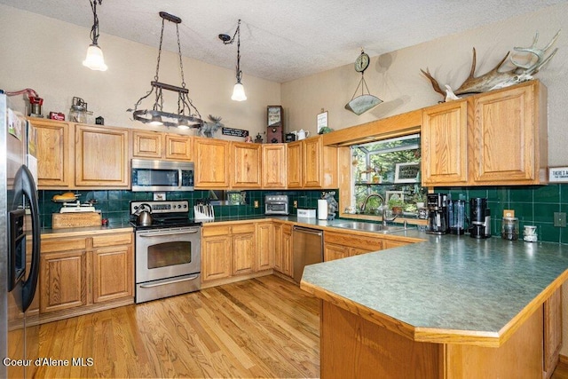 kitchen with appliances with stainless steel finishes, a sink, a textured ceiling, a peninsula, and tasteful backsplash