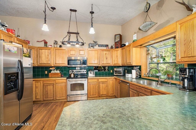 kitchen with a sink, a textured ceiling, stainless steel appliances, wood finished floors, and tasteful backsplash