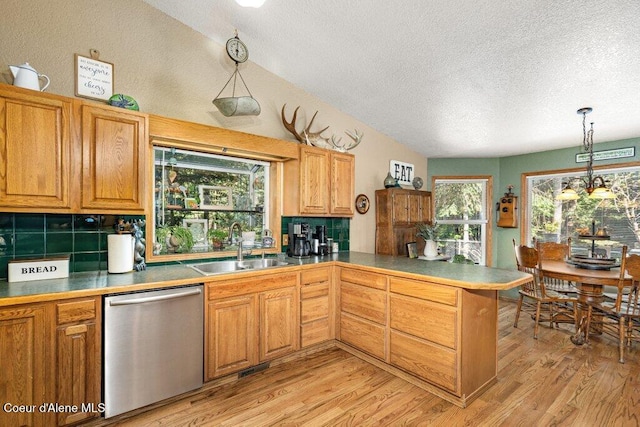 kitchen featuring a sink, dishwasher, a textured ceiling, light wood-style flooring, and a peninsula