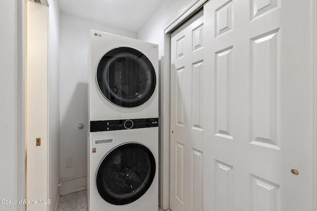 laundry area featuring light tile patterned floors, baseboards, and stacked washer and dryer
