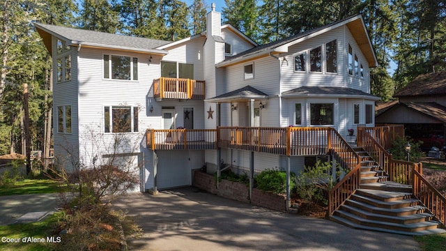 view of front of home featuring a balcony, a chimney, stairs, an attached garage, and driveway