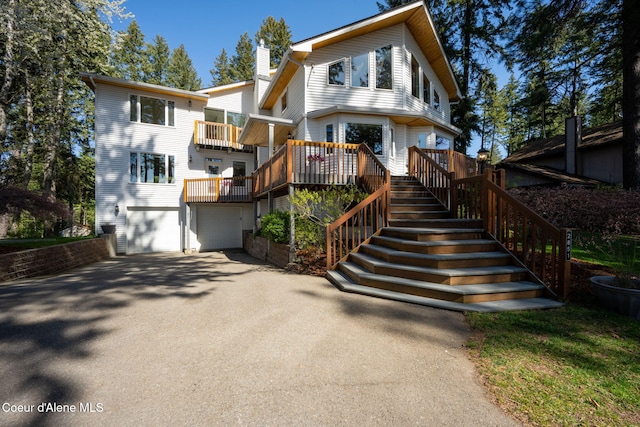 view of front of property featuring a chimney, stairway, a balcony, aphalt driveway, and an attached garage