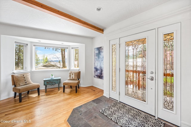 doorway to outside with baseboards, a textured ceiling, wood finished floors, and beamed ceiling