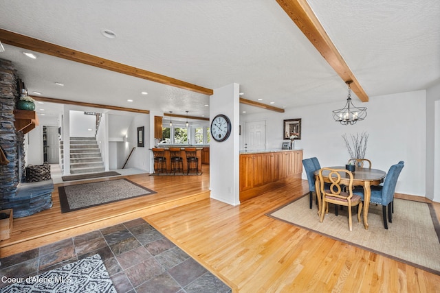 dining space with a textured ceiling, baseboards, wood finished floors, beamed ceiling, and stairway